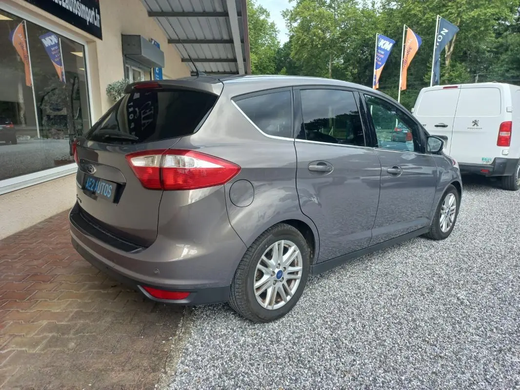 Ford C-MAX gris vue 3/4 arrière droit, avec vitres teintées et jantes alliage, stationné sur gravier.