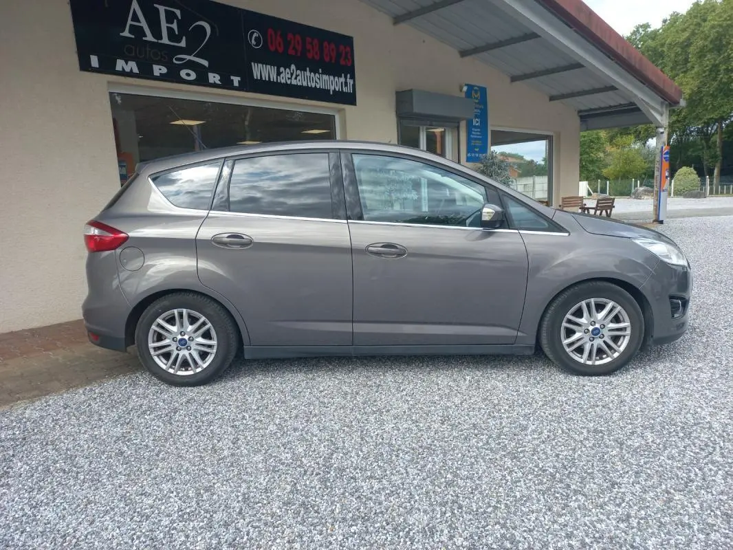Vue de profil côté droit d'une Ford C-MAX gris métallisé de 2015, stationnée devant un bâtiment commercial.