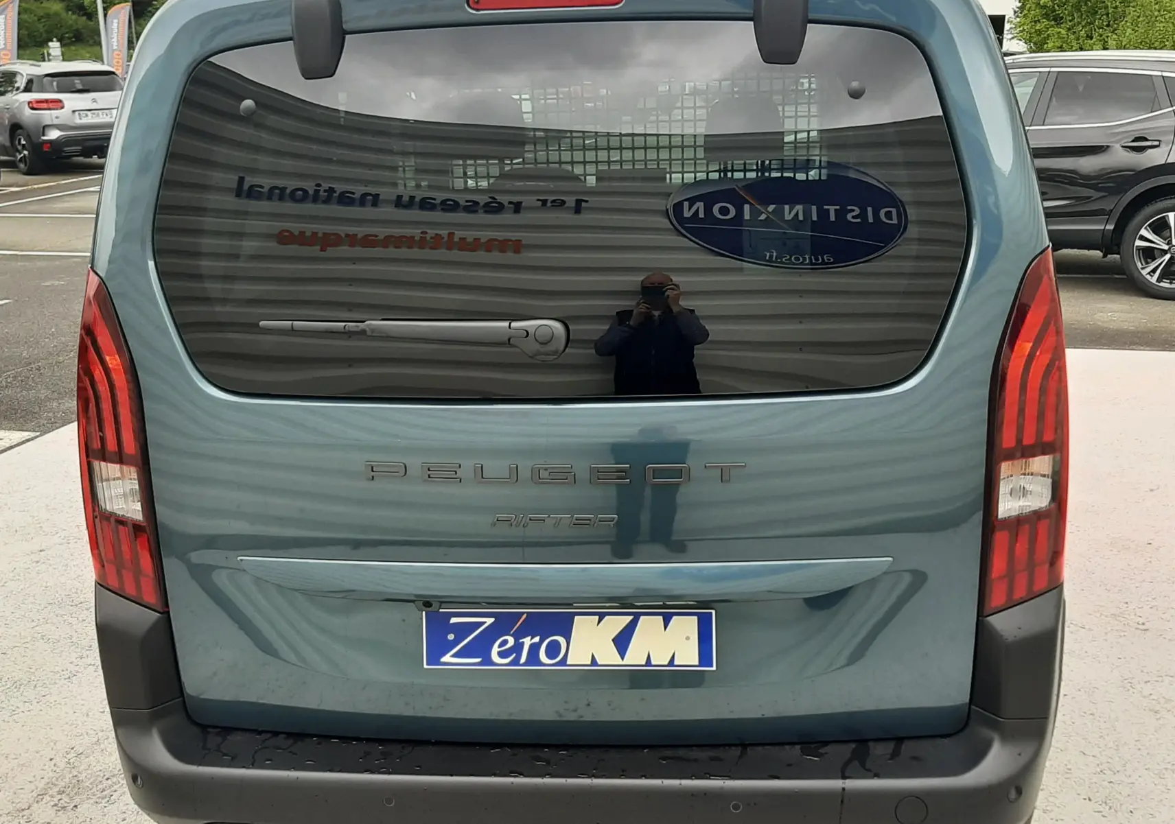Vue arrière d'un Peugeot Rifter bleu Kiama 2026 avec lunette arrière ouvrante et feux verticaux rouges.