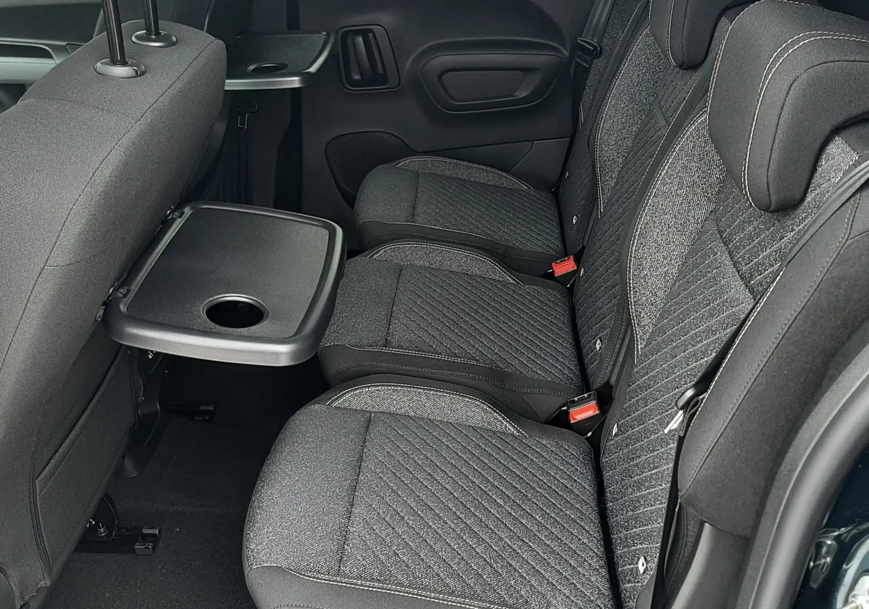 Vue latérale intérieure des sièges arrière en tissu gris du Peugeot Rifter Bleu Kiama avec tablette rabattable intégrée.