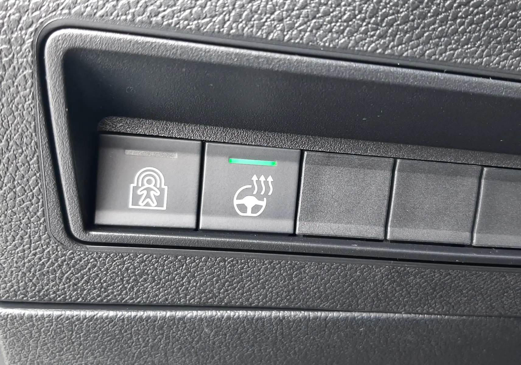 Boutons de commande du volant chauffant et de la sécurité enfants sur le tableau de bord noir du Peugeot Rifter bleu Kiama.