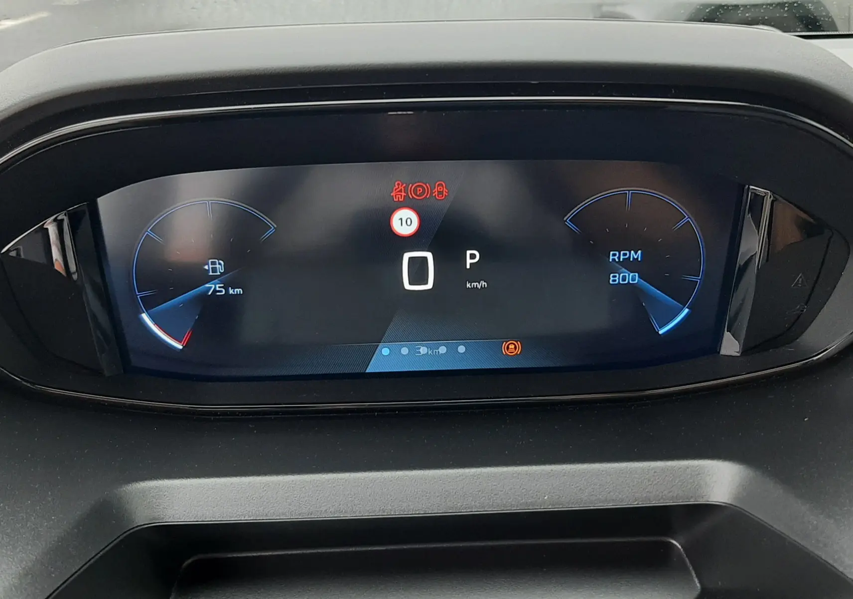 Vue rapprochée du tableau de bord numérique du Peugeot Rifter gris acier, affichant 0 km/h et 75 km d'autonomie restante.