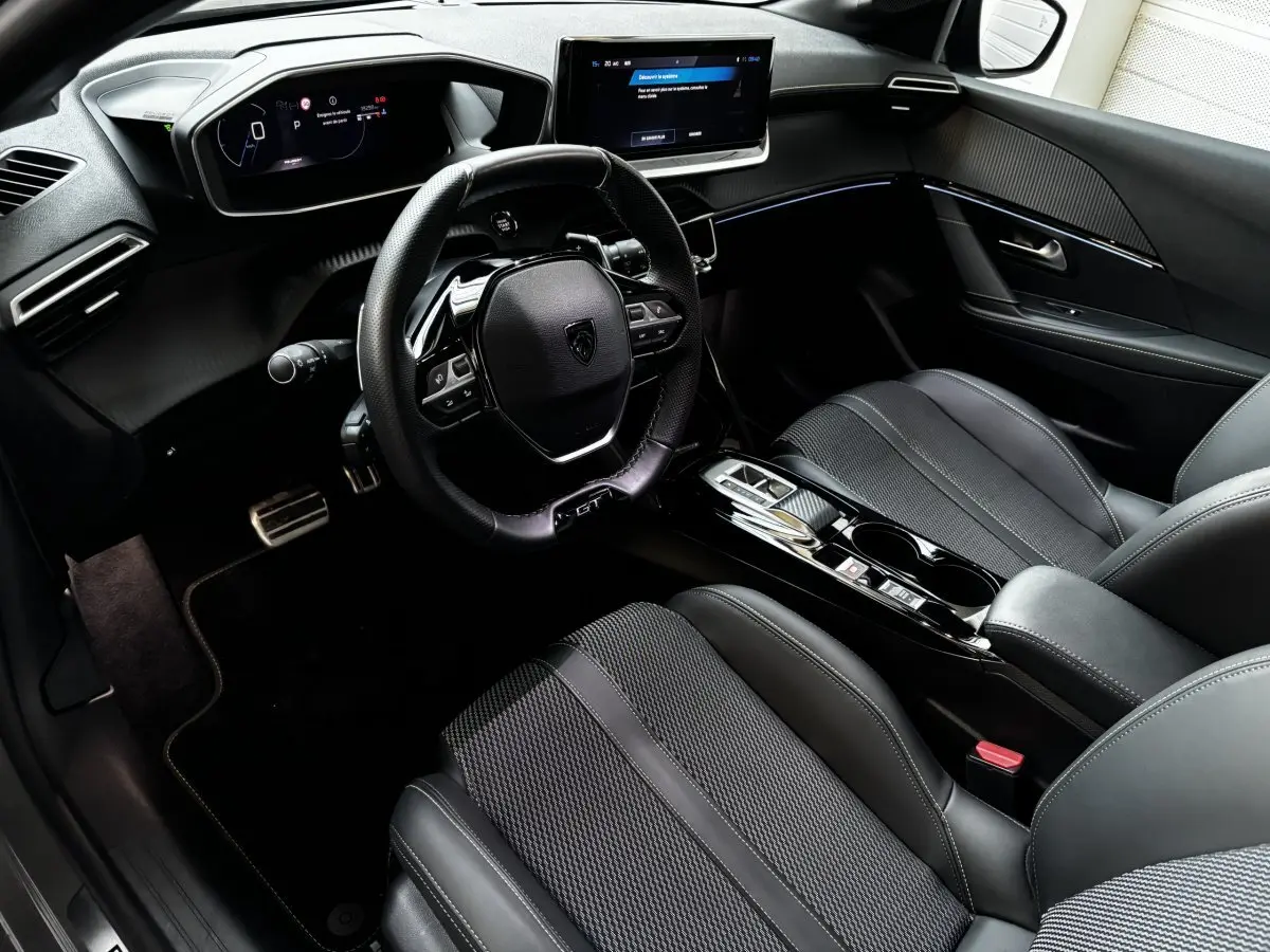 Intérieur Peugeot 208 Hybrid 136 GT vu côté conducteur, avec tableau de bord numérique et finitions noires élégantes.