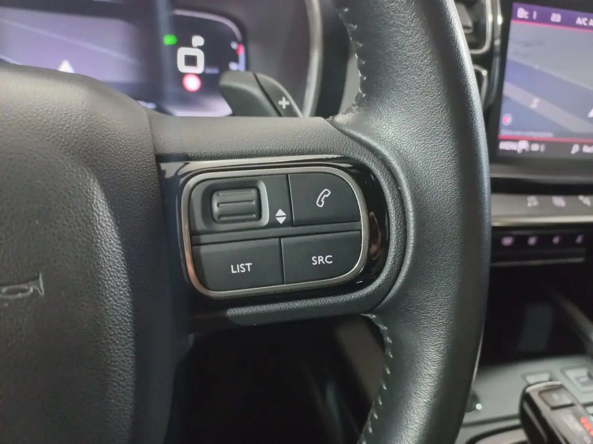 Gros plan sur les commandes gauche du volant cuir noir du Citroën C5 Aircross 2020 avec écran tactile en arrière-plan.