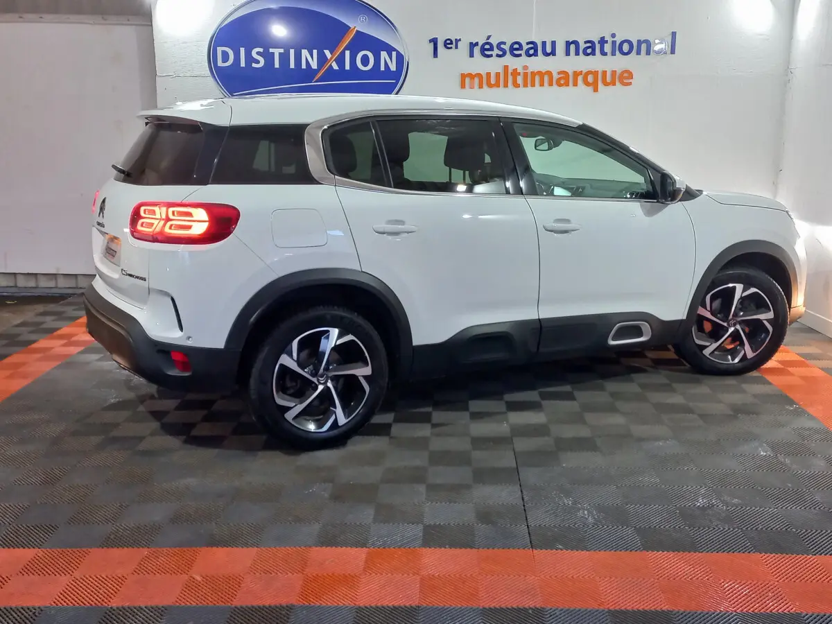Vue de profil côté gauche d'un Citroën C5 Aircross blanc avec feux arrière allumés en intérieur showroom.