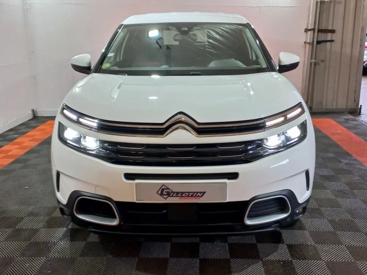 Vue de face d'un Citroën C5 Aircross blanc avec phares allumés et calandre distinctive dans un garage.