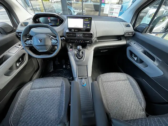 Vue intérieure avant du Peugeot Rifter 2024 gris foncé, montrant le volant multifonction, la boîte manuelle et l’écran central tactile.