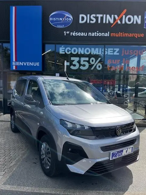 Vue 3/4 avant d'un Peugeot Rifter gris foncé stationné devant une concession avec logo Distinxion visible.