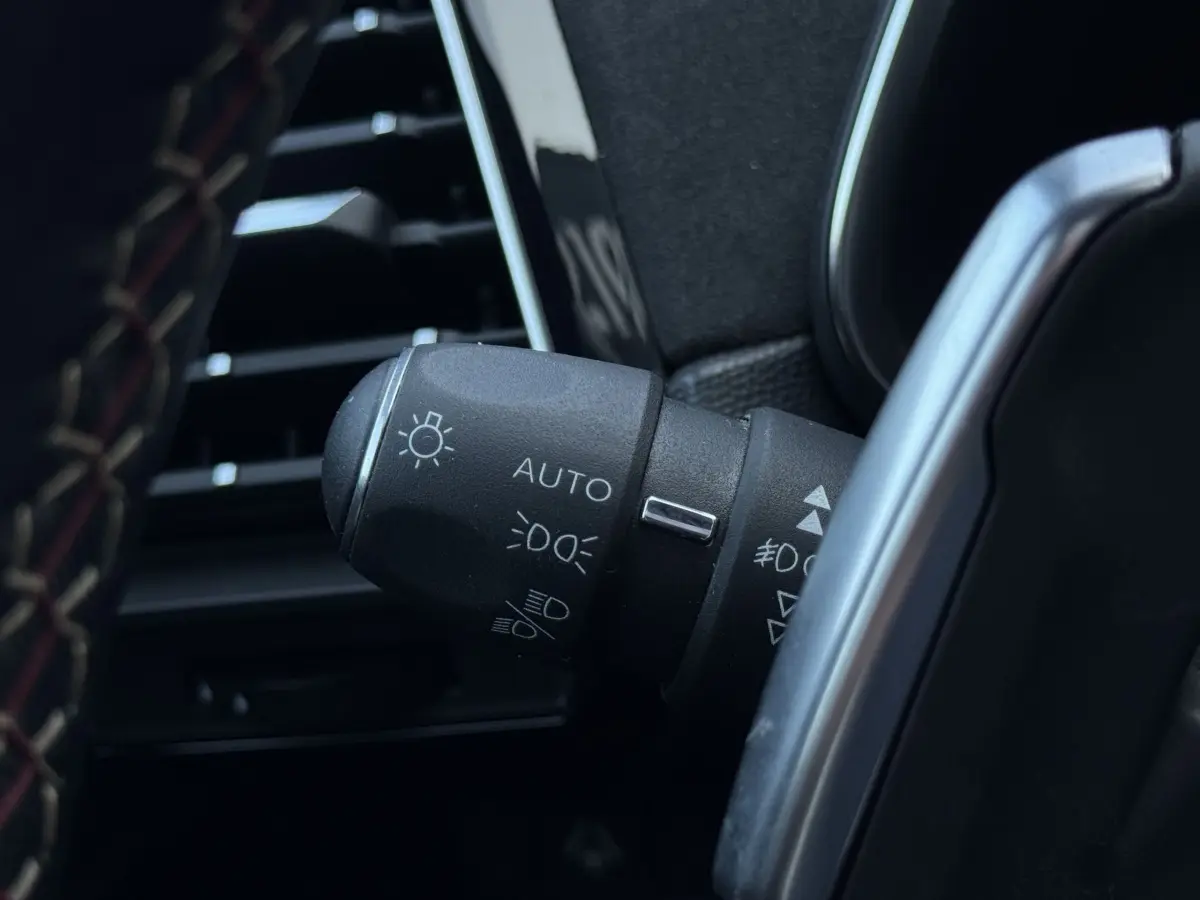 Gros plan sur la commande des phares automatique dans l’habitacle noir du DS7 Crossback blanc, côté gauche du volant.