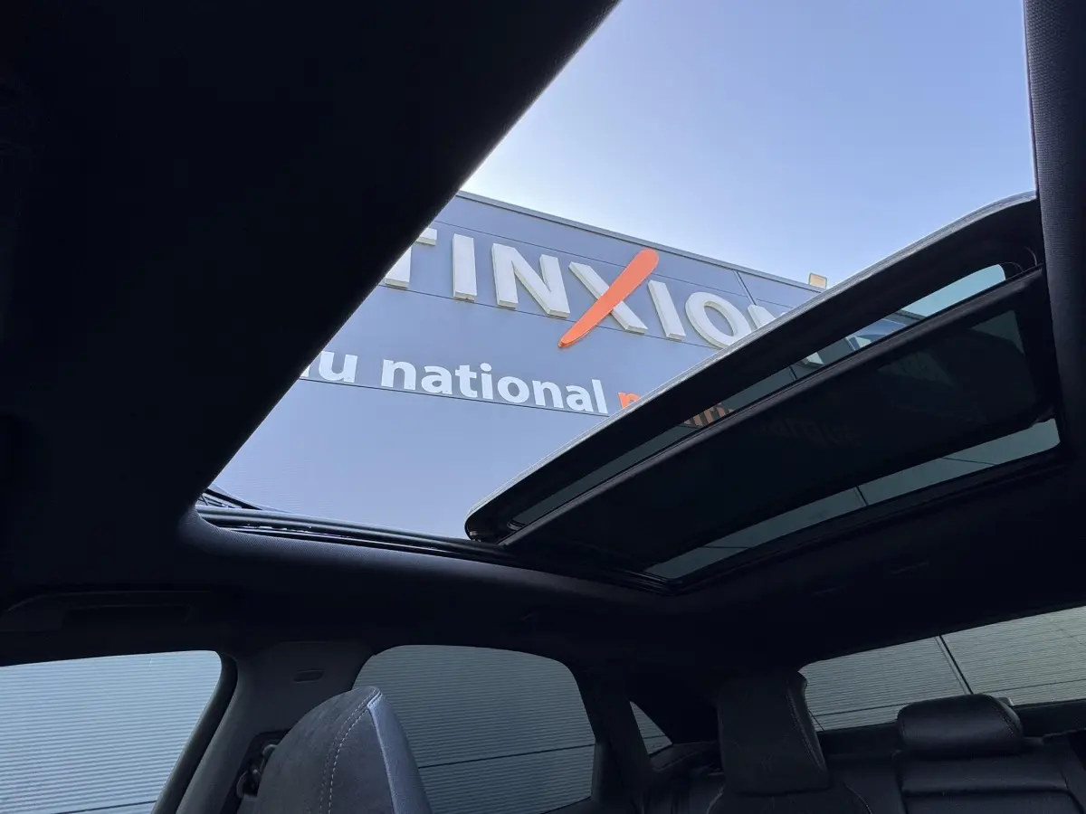 Vue intérieure du toit ouvrant panoramique ouvert du DS7 Crossback blanc, avec sièges arrière en cuir noir visibles.