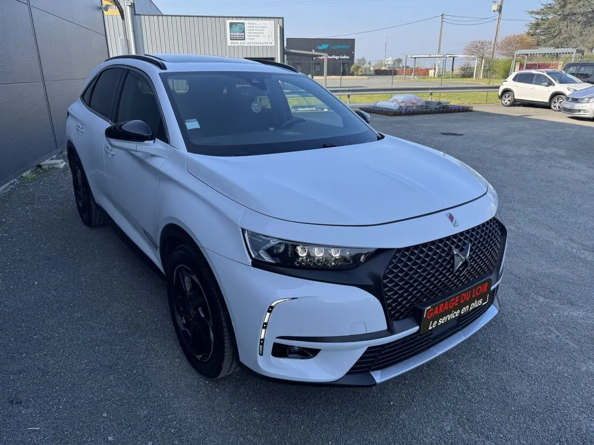 DS7 Crossback blanc vue 3/4 avant droit, calandre noire distinctive et phares LED modernes, stationné en extérieur.