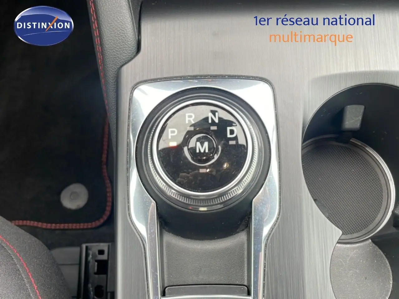 Gros plan sur la molette de boîte automatique du Ford Kuga 2024, avec console grise et surpiqûres rouges visibles.