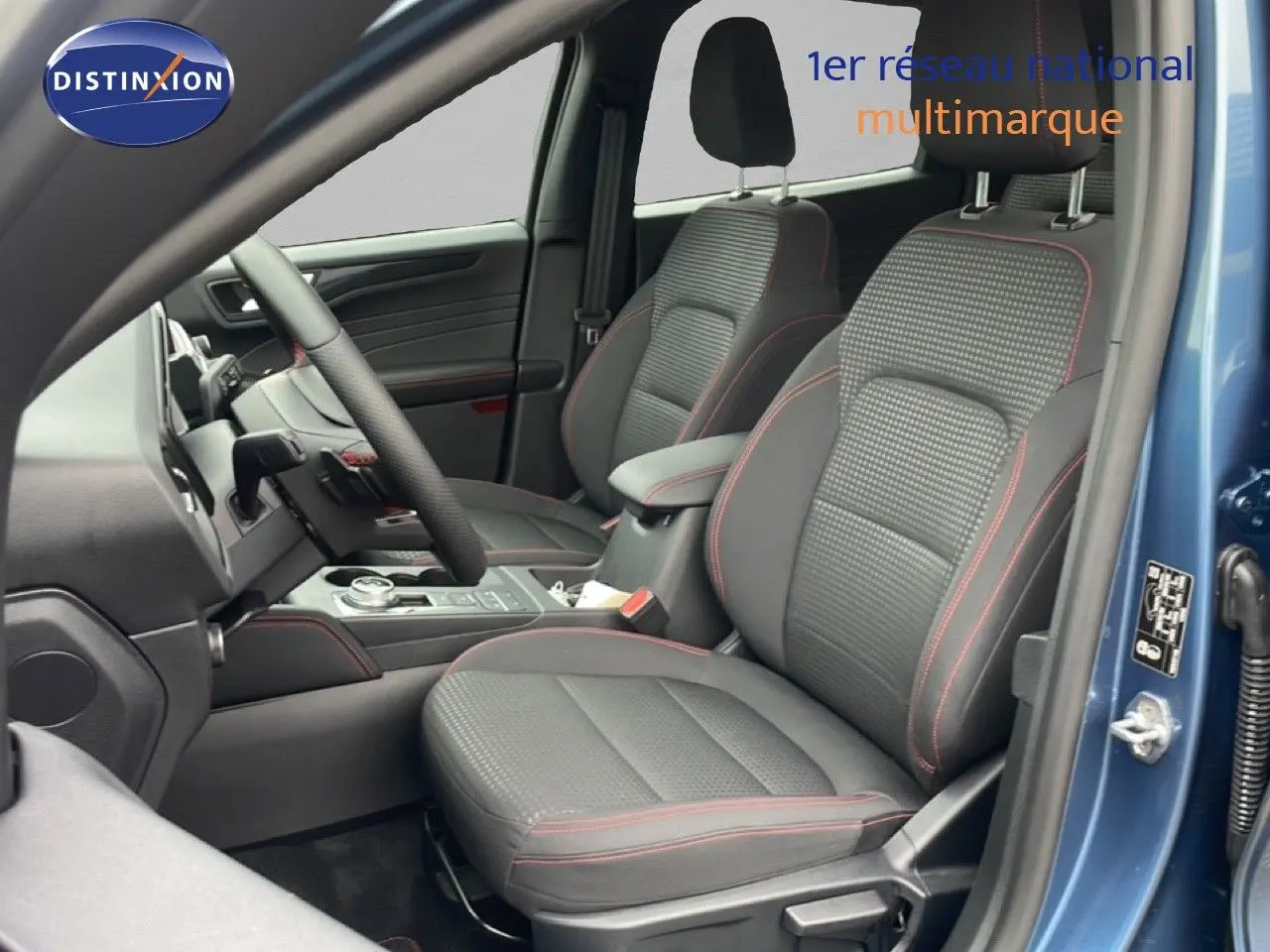 Vue intérieure côté conducteur du Ford Kuga bleu chrome métal 2024, sièges tissu noir avec surpiqûres rouges.