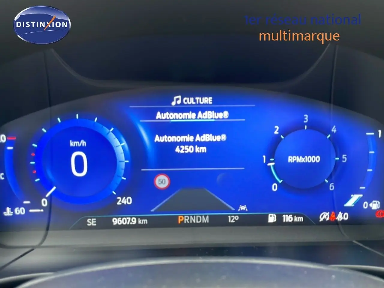 Vue rapprochée du tableau de bord numérique bleu du Ford Kuga 2024 affichant la vitesse, le régime et l'autonomie AdBlue.