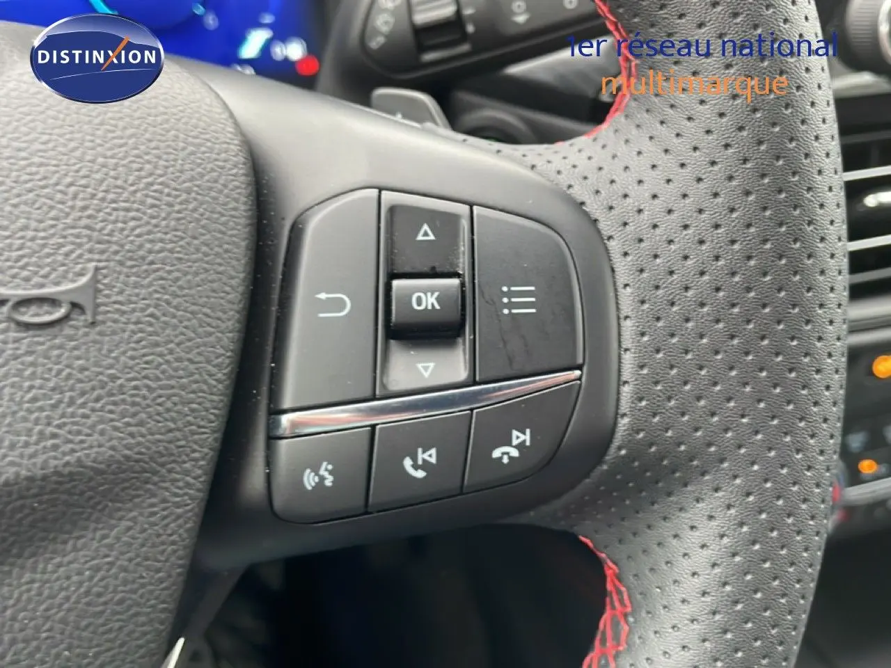 Gros plan sur le volant en cuir noir perforé avec surpiqûres rouges du Ford Kuga 2024, boutons de commande visibles.