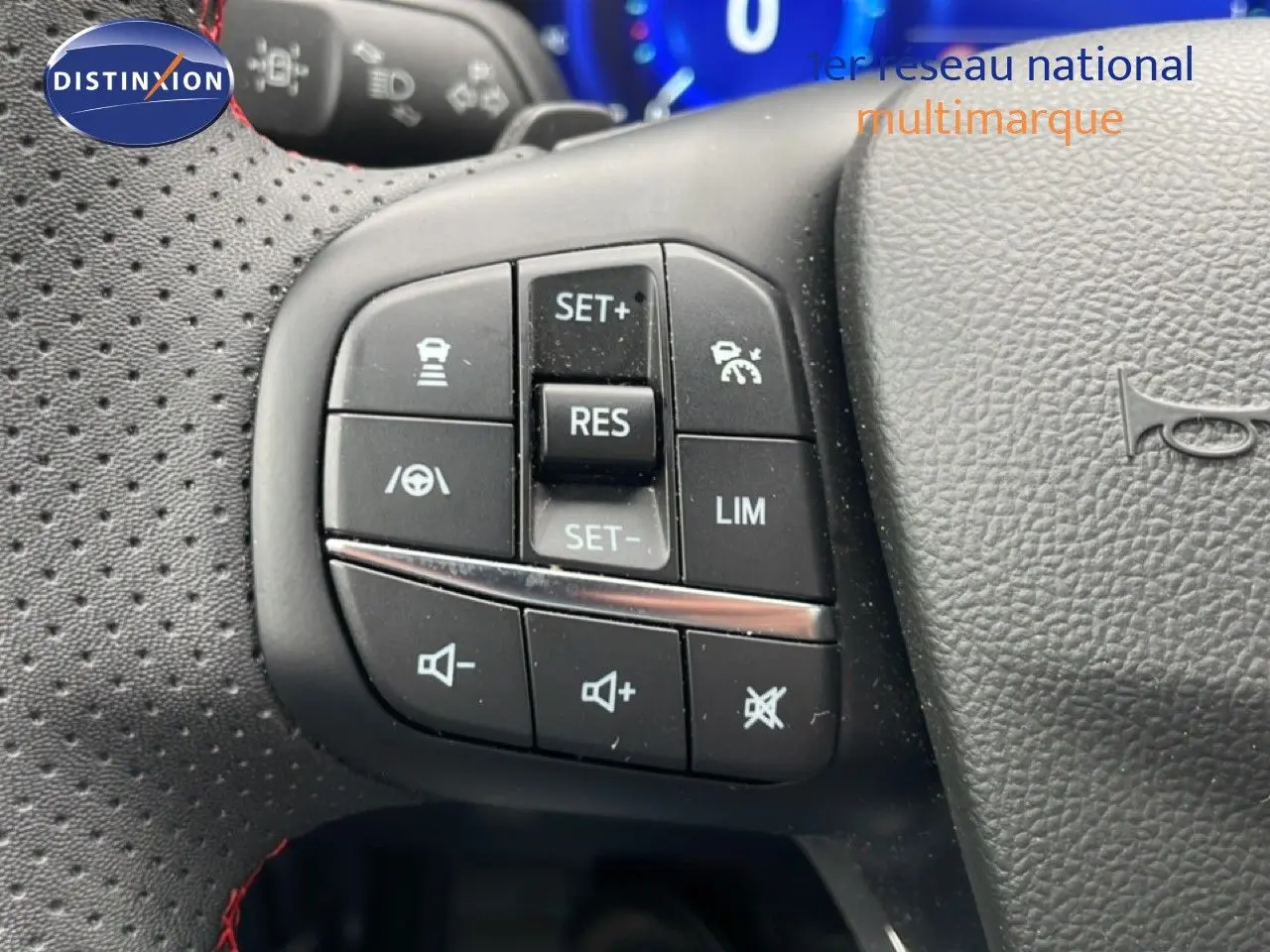Gros plan sur les commandes au volant côté gauche du Ford Kuga bleu chrome 2024, avec boutons de régulateur et volume sonore.