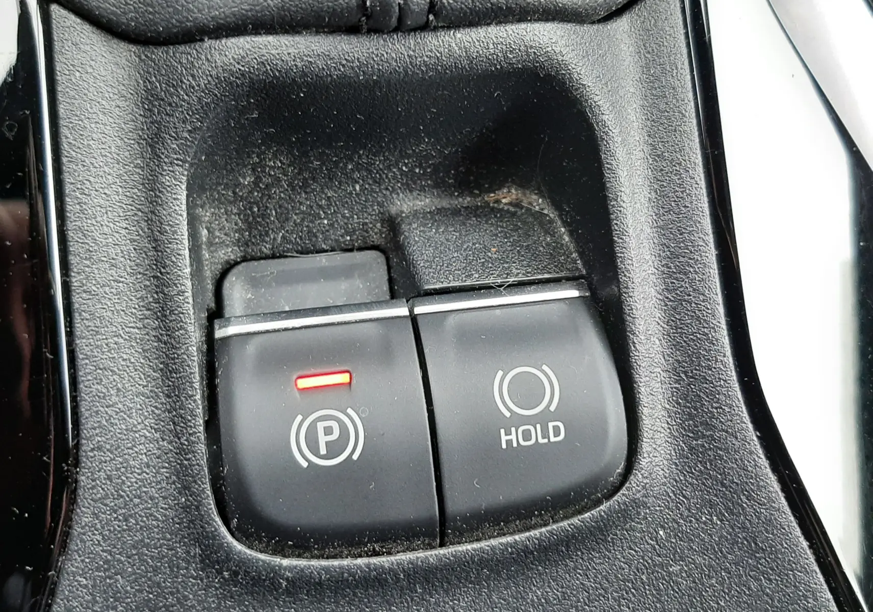 Gros plan sur les boutons de frein à main électronique et hold dans l'habitacle noir d'une Toyota Corolla blanche 2022.