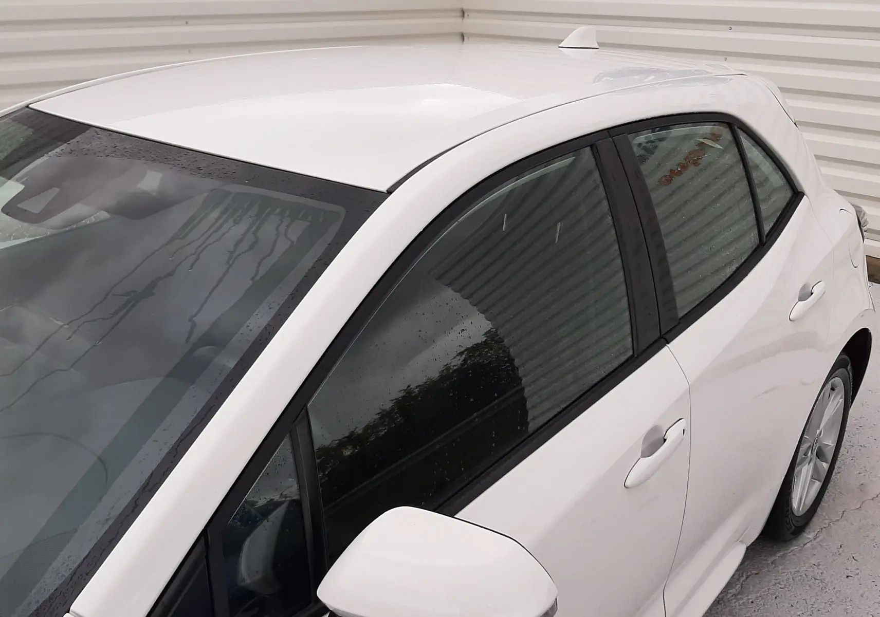 Vue de côté droit en plongée d'une Toyota Corolla blanche 2022, mettant en valeur les vitres teintées et le rétroviseur intégré.