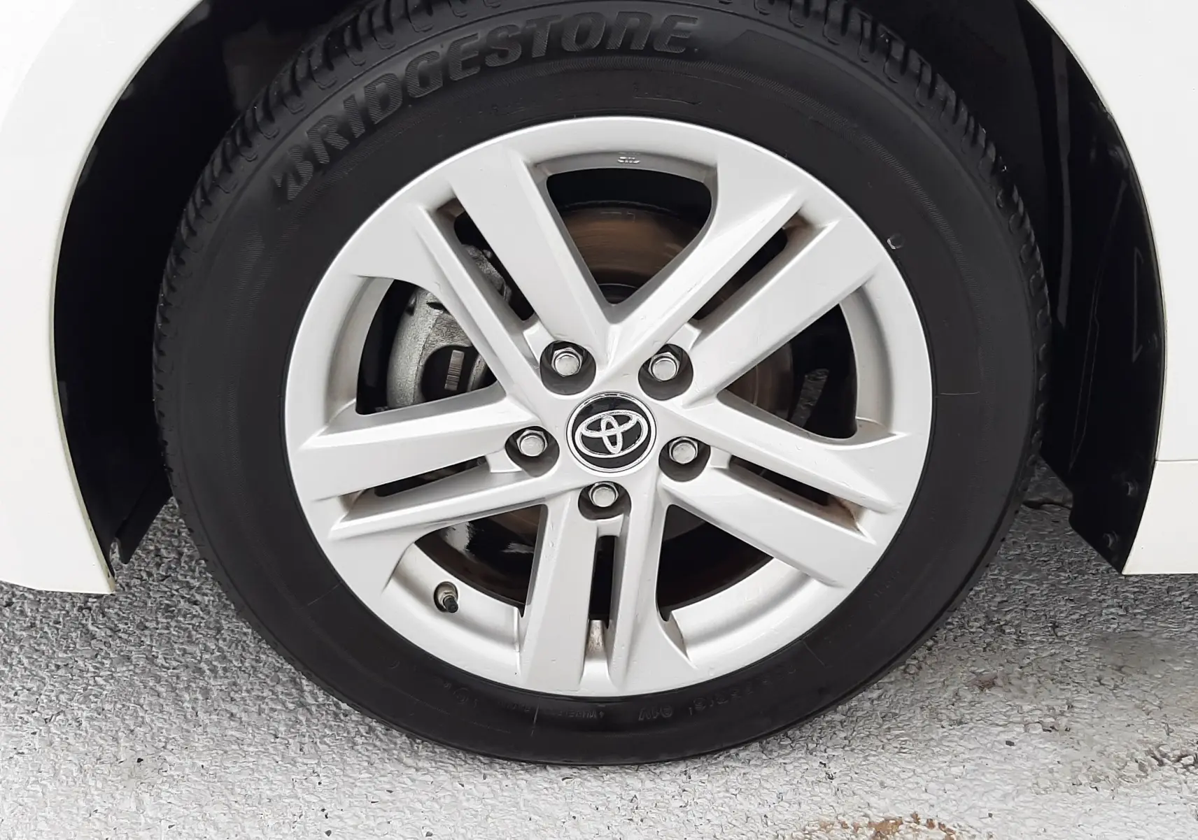 Gros plan sur la roue avant droite blanche d'une Toyota Corolla 122 CH Dynamic avec jante alliage et logo Toyota central.