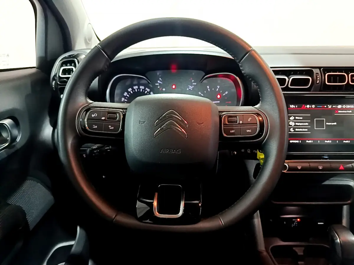 Vue rapprochée du volant cuir noir du Citroën C3 Aircross 2019 avec commandes intégrées et tableau de bord éclairé.
