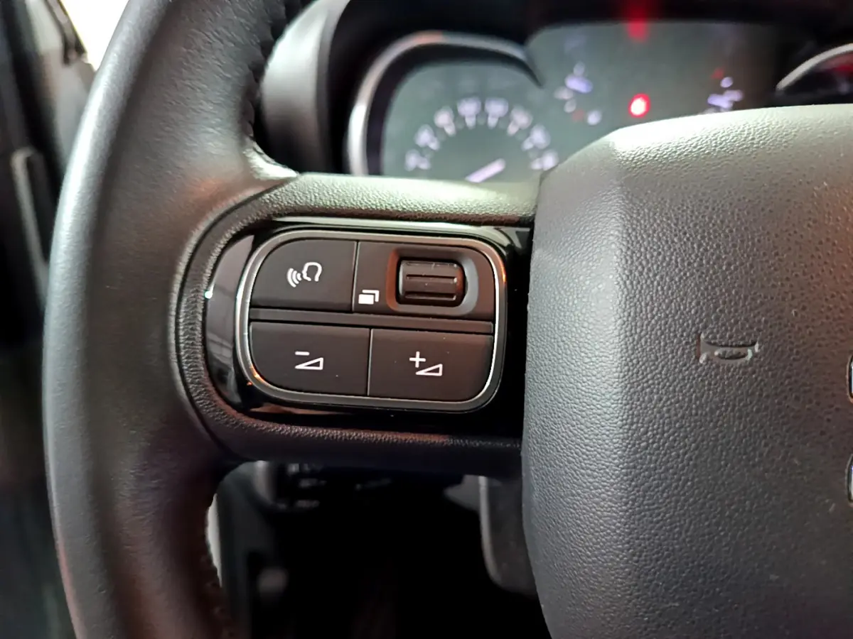 Gros plan sur le côté gauche du volant cuir noir du Citroën C3 Aircross blanc, avec commandes audio intégrées.