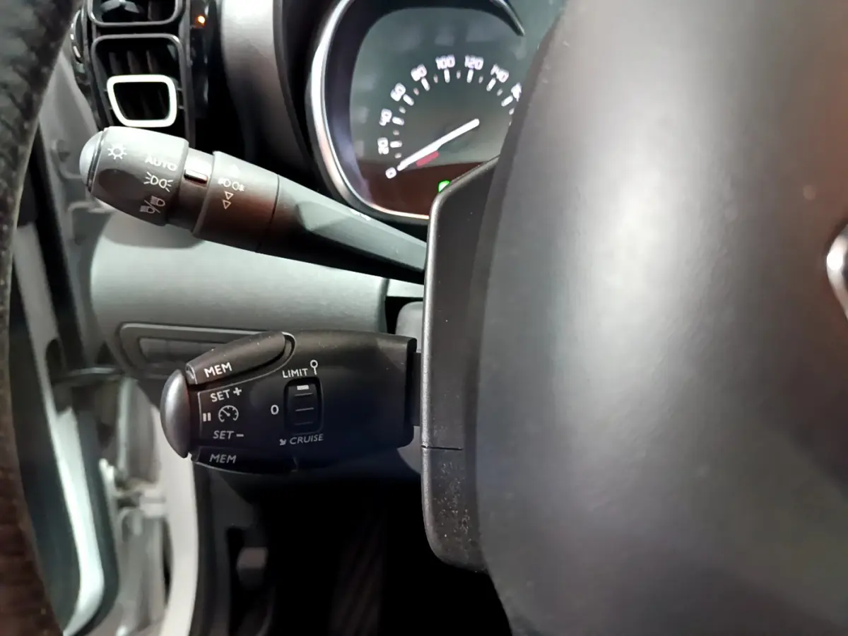 Gros plan sur la commande de régulateur de vitesse à gauche du volant cuir d'une Citroën C3 Aircross blanche de 2019.