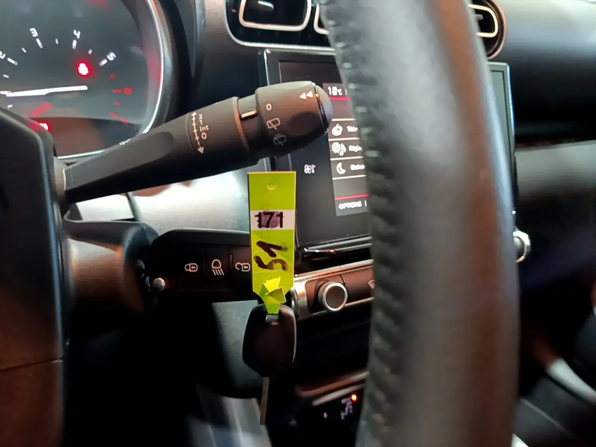 Gros plan sur la colonne de direction et le volant cuir noir d'une Citroën C3 Aircross blanche, tableau de bord en arrière-plan.