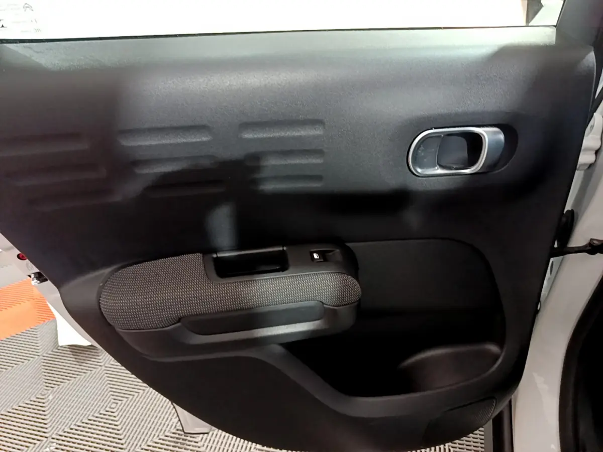 Intérieur de la porte arrière droite noire du Citroën C3 Aircross blanc, avec poignée et bouton de vitre électrique.