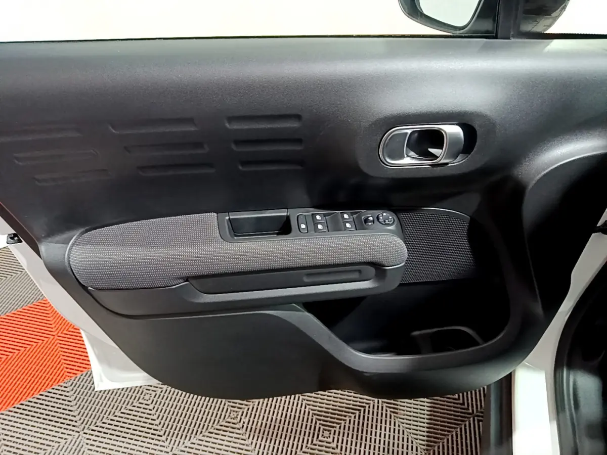 Vue rapprochée de la porte avant gauche noire et grise du Citroën C3 Aircross blanc, avec commandes électriques et poignée chromée.