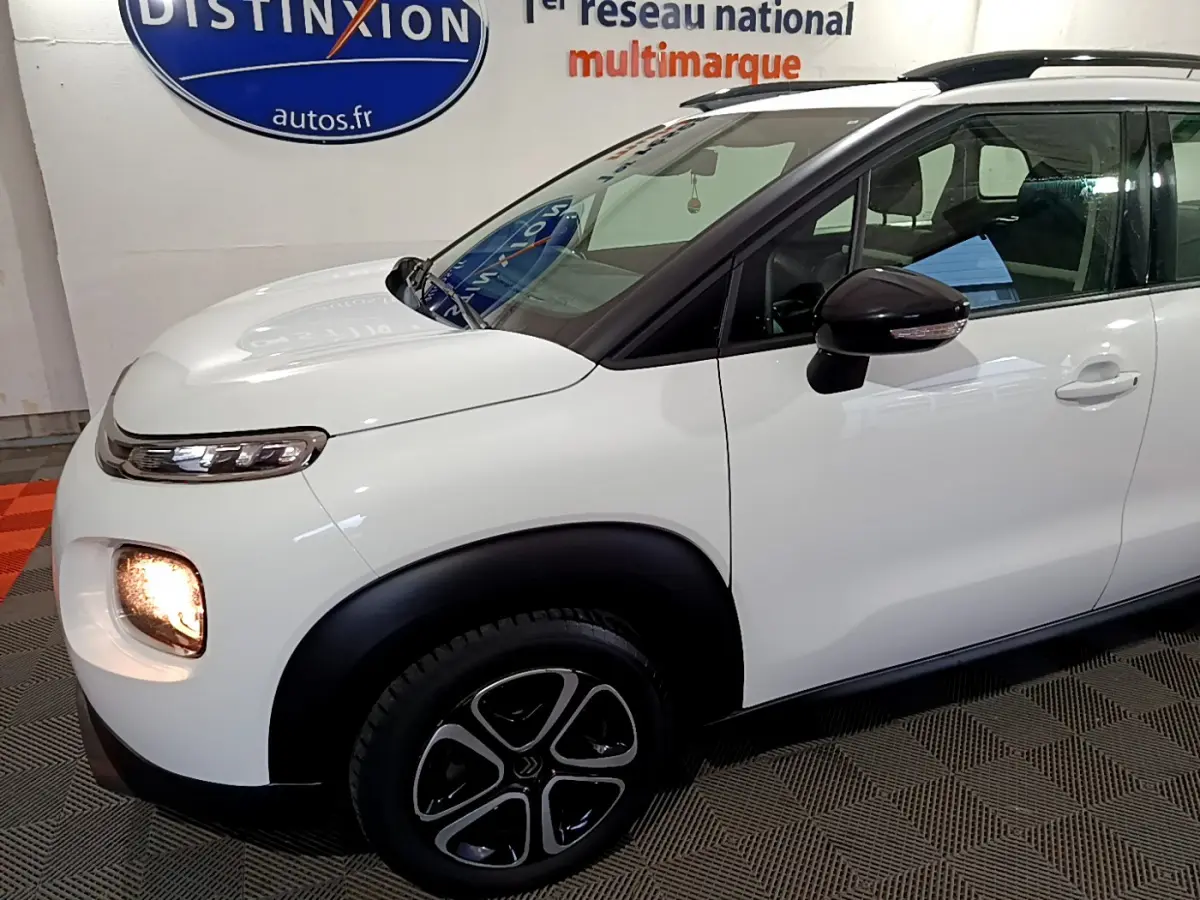 Vue de profil avant droit d'un Citroën C3 Aircross blanc avec feux allumés et rétroviseur noir brillant.