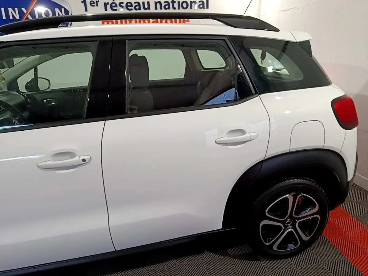 Vue latérale droite d'un Citroën C3 Aircross blanc avec toit noir et jantes distinctives en intérieur showroom.