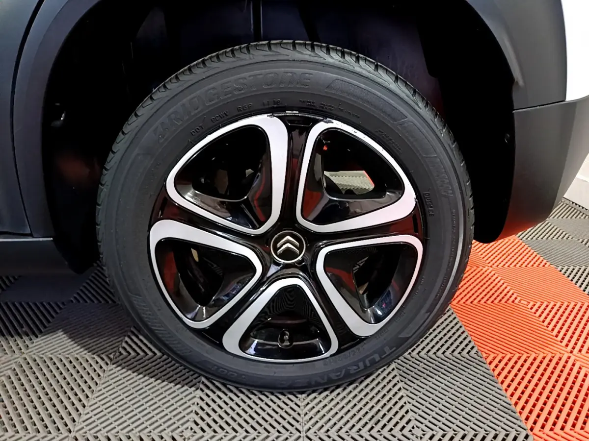 Gros plan sur la roue avant droite du Citroën C3 Aircross blanc, mettant en valeur la jante noire et argentée au design moderne.