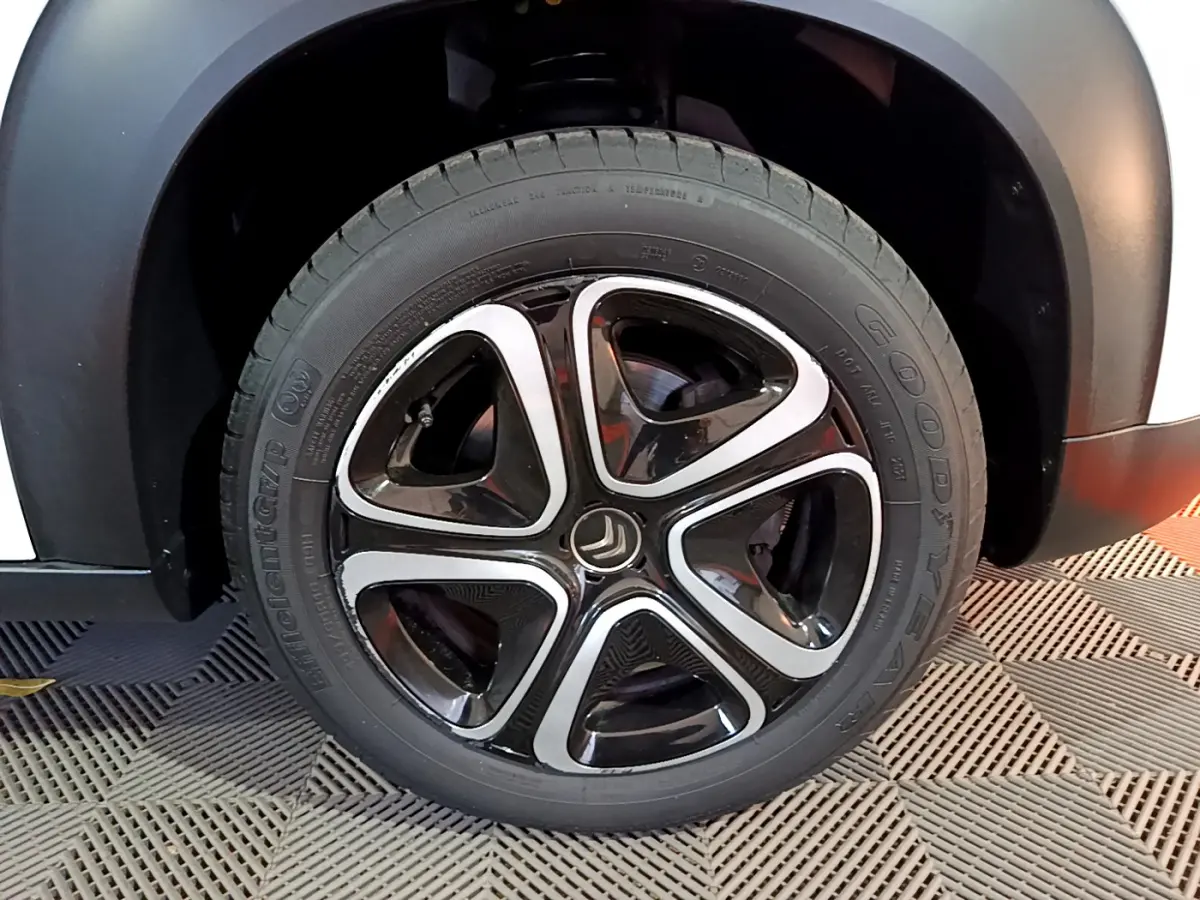 Gros plan sur la roue avant droite d'une Citroën C3 Aircross blanche, jante alliage noire et argentée au design moderne.