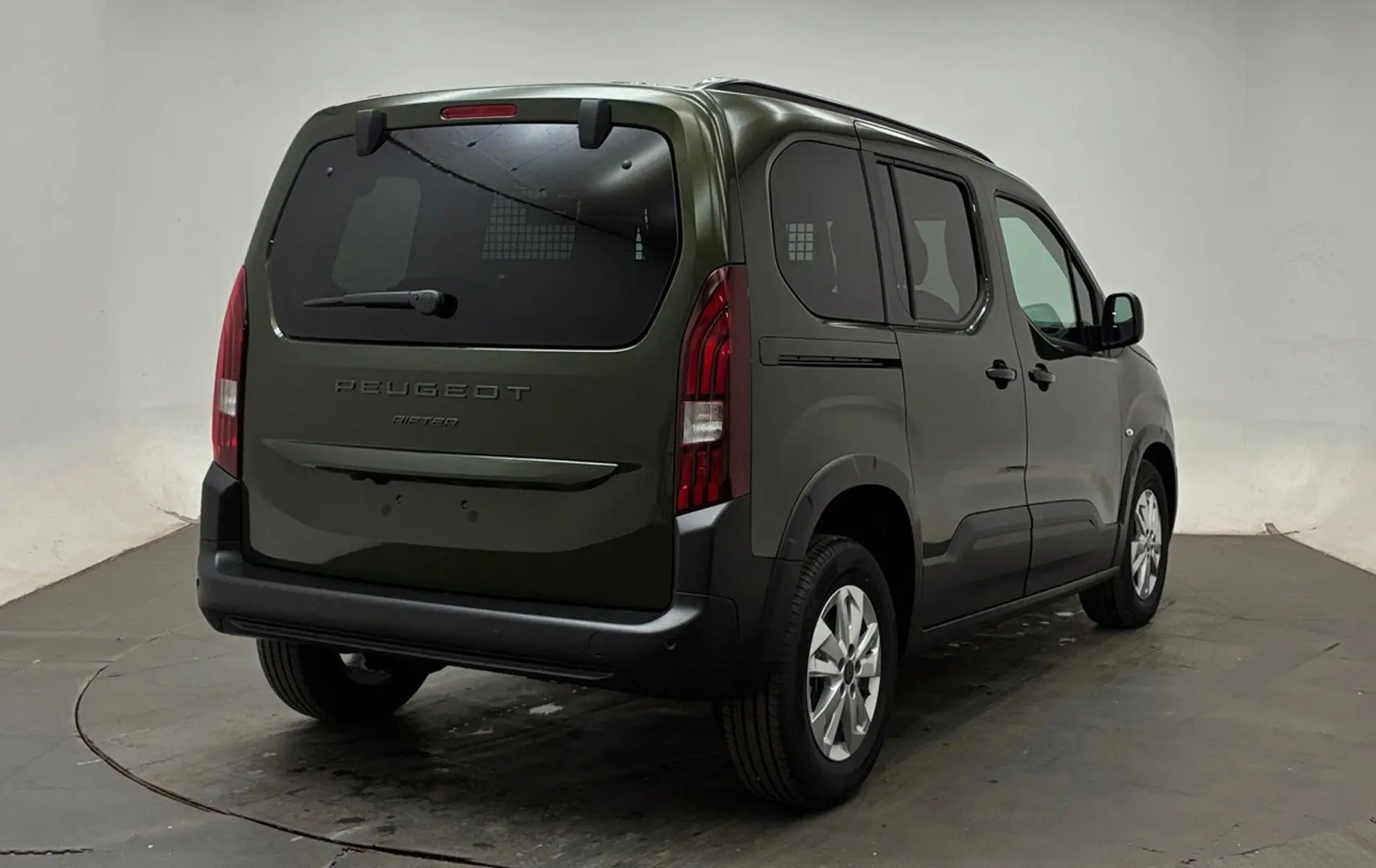 Vue 3/4 arrière droite d’un Peugeot Rifter 2026 vert Sirkka avec vitres arrière surteintées et jantes alliage.