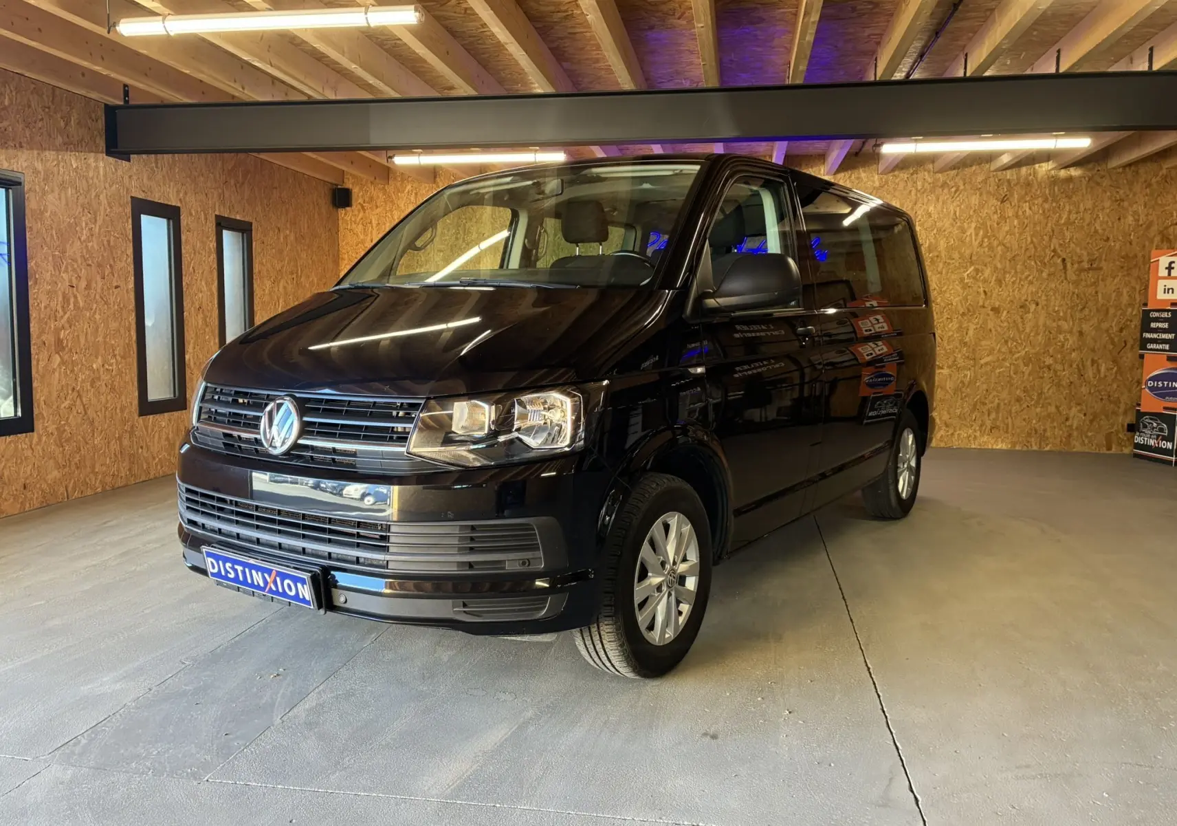 Volkswagen Multivan T6 noir vu en 3/4 avant droit dans un garage avec éclairage intérieur chaud.