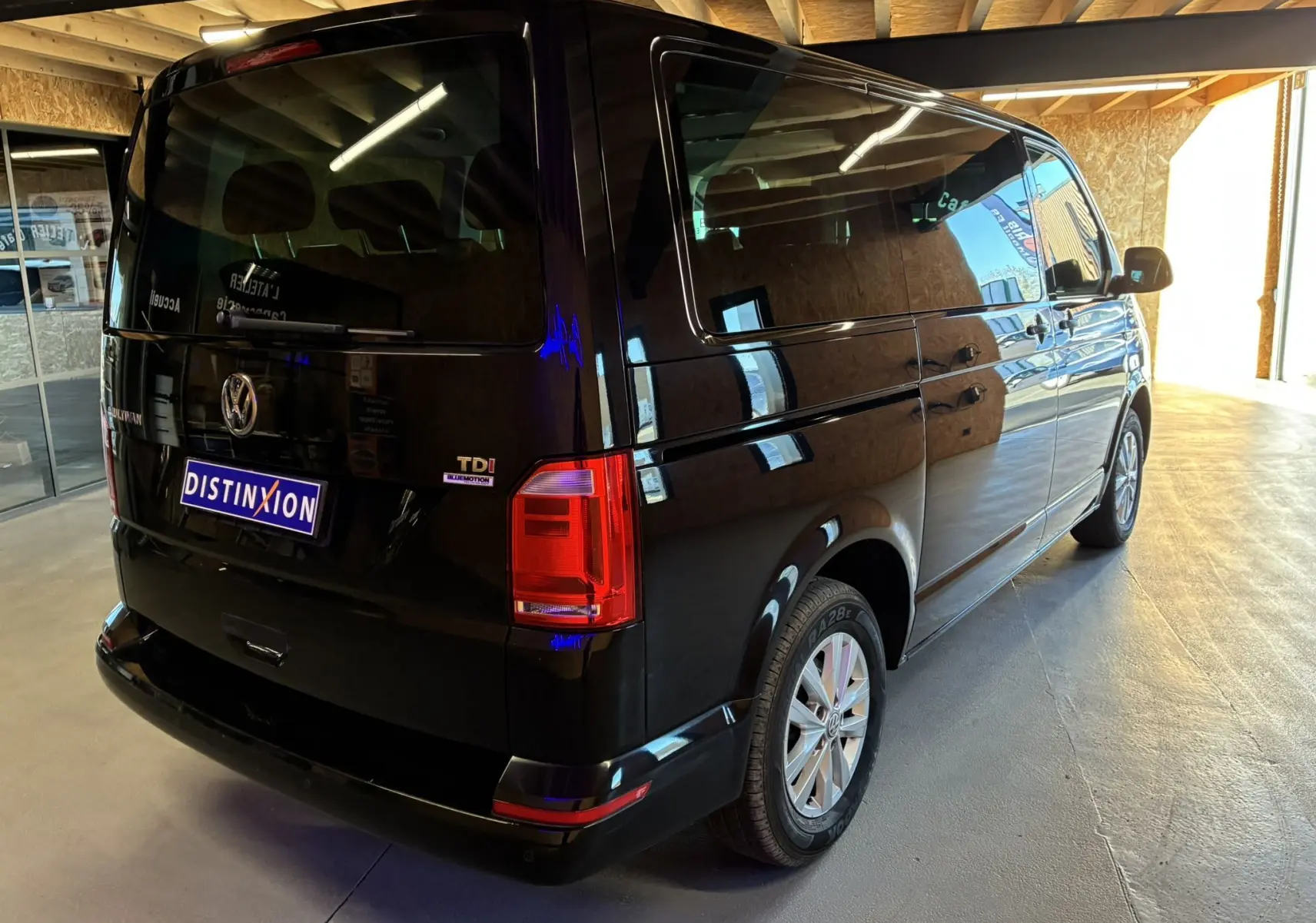 Volkswagen Multivan T6 noir vu en 3/4 arrière droit dans un garage avec vitres teintées et feux rouges.