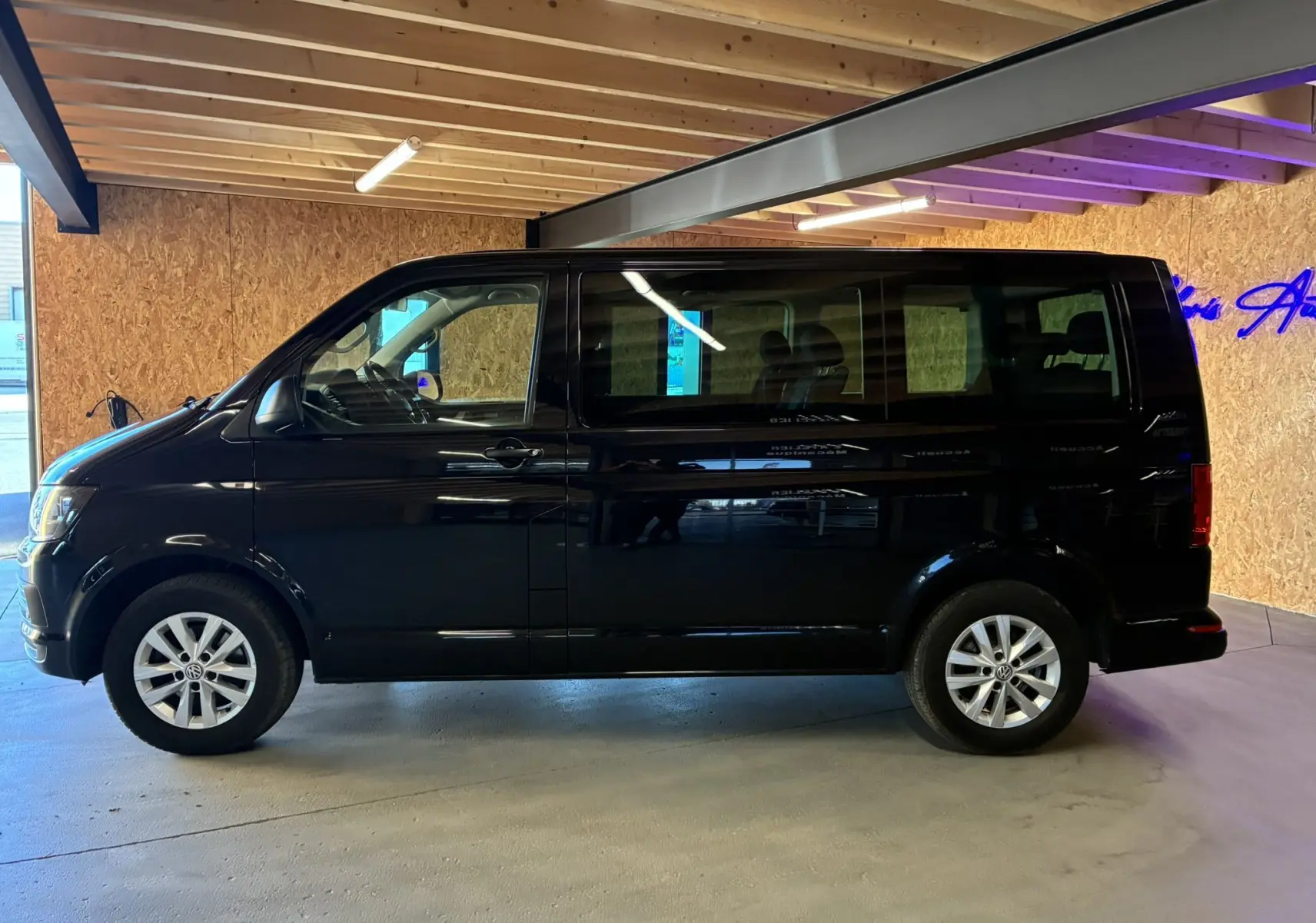 Vue de profil côté gauche d’un Volkswagen Multivan T6 noir de 2015 stationné en intérieur avec jantes alliage visibles.