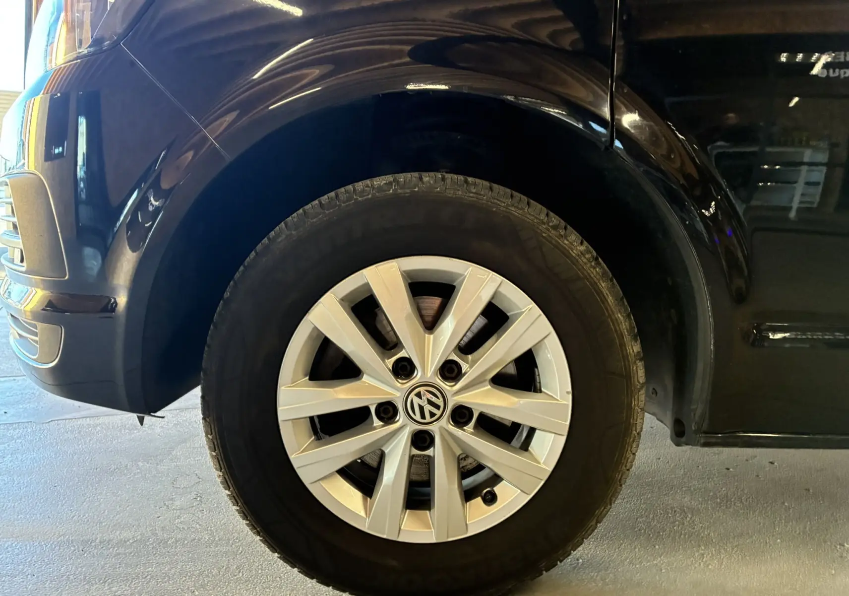 Gros plan sur la roue avant gauche d’un Volkswagen Multivan noir T6 PH.1 avec jante alliage argentée.