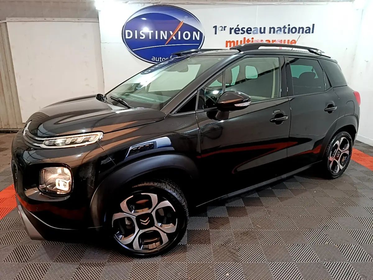Citroën C3 Aircross noir vue 3/4 avant droit en intérieur, avec jantes distinctives et barres de toit noires.