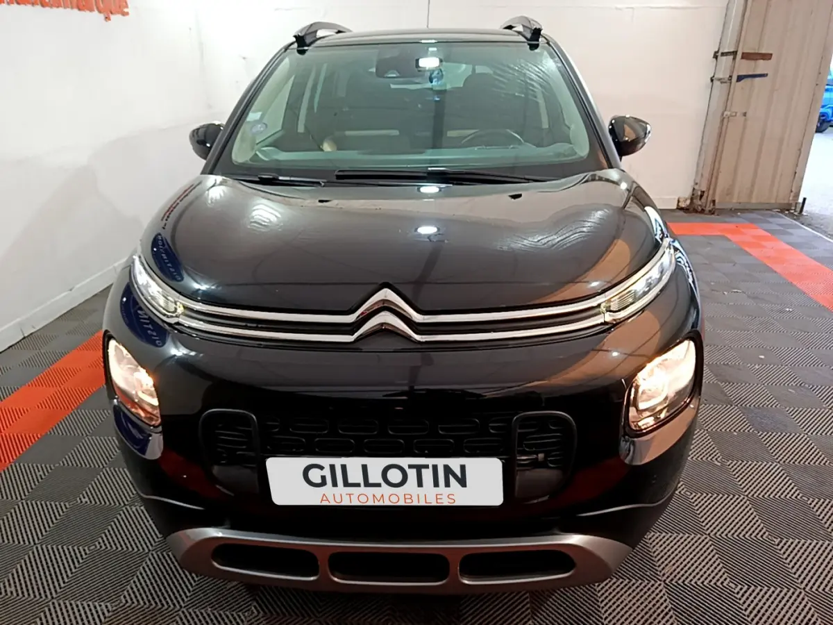 Vue avant d'un Citroën C3 Aircross noir avec phares allumés et barres de toit visibles en intérieur showroom.