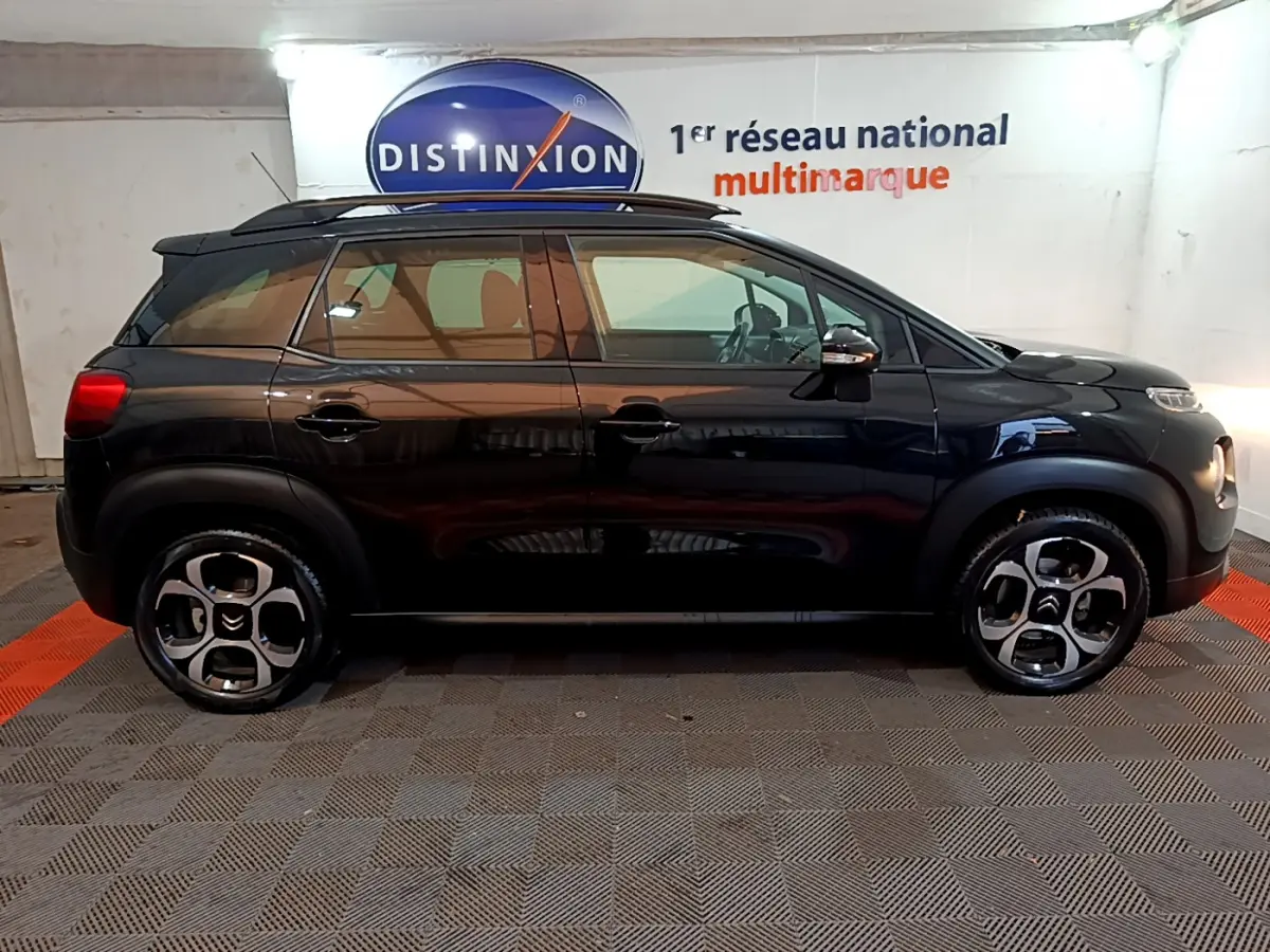Profil latéral droit d'un Citroën C3 Aircross noir 2019 avec barres de toit et jantes distinctives en intérieur showroom.