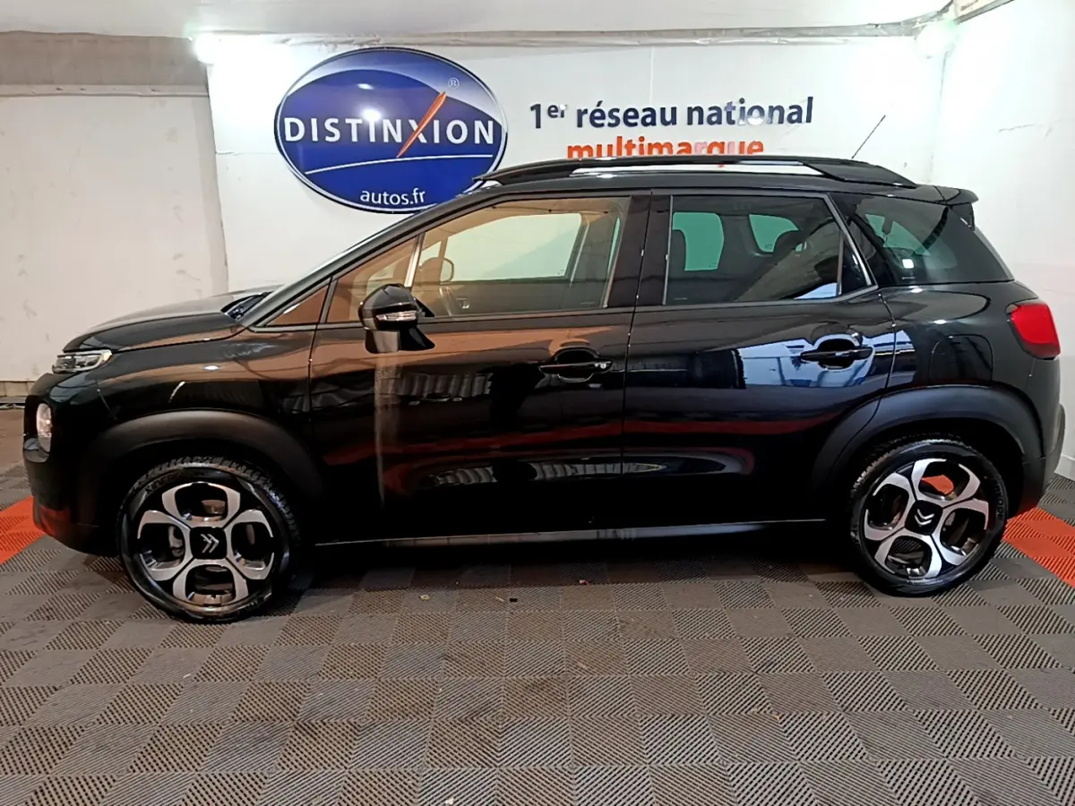 Profil côté gauche d'un Citroën C3 Aircross noir 2019 avec jantes originales et barres de toit noires visibles en intérieur showroom.