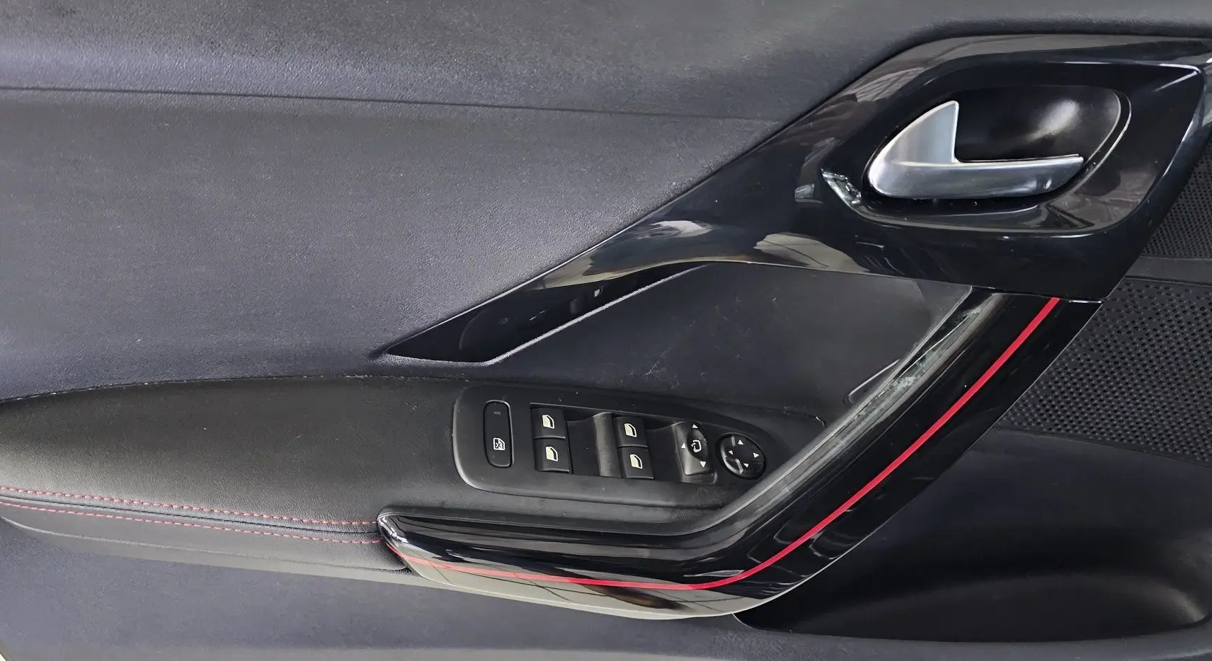 Gros plan sur la porte intérieure côté conducteur de la Peugeot 208 GT-LINE noire avec surpiqûres rouges et commandes électriques.