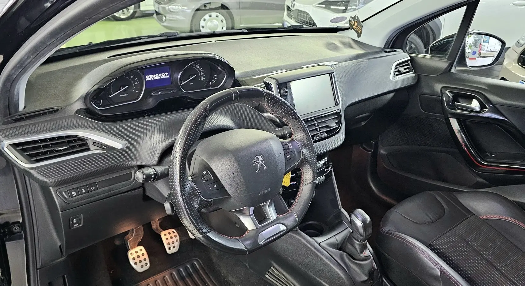 Vue intérieure côté conducteur de la Peugeot 208 GT-LINE 2015 noire, volant cuir, tableau de bord et écran tactile visibles.