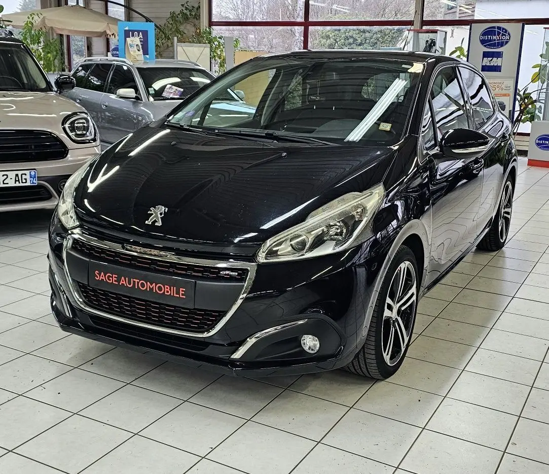Peugeot 208 GT-LINE noire vue 3/4 avant en intérieur, avec jantes alliage et calandre chromée.