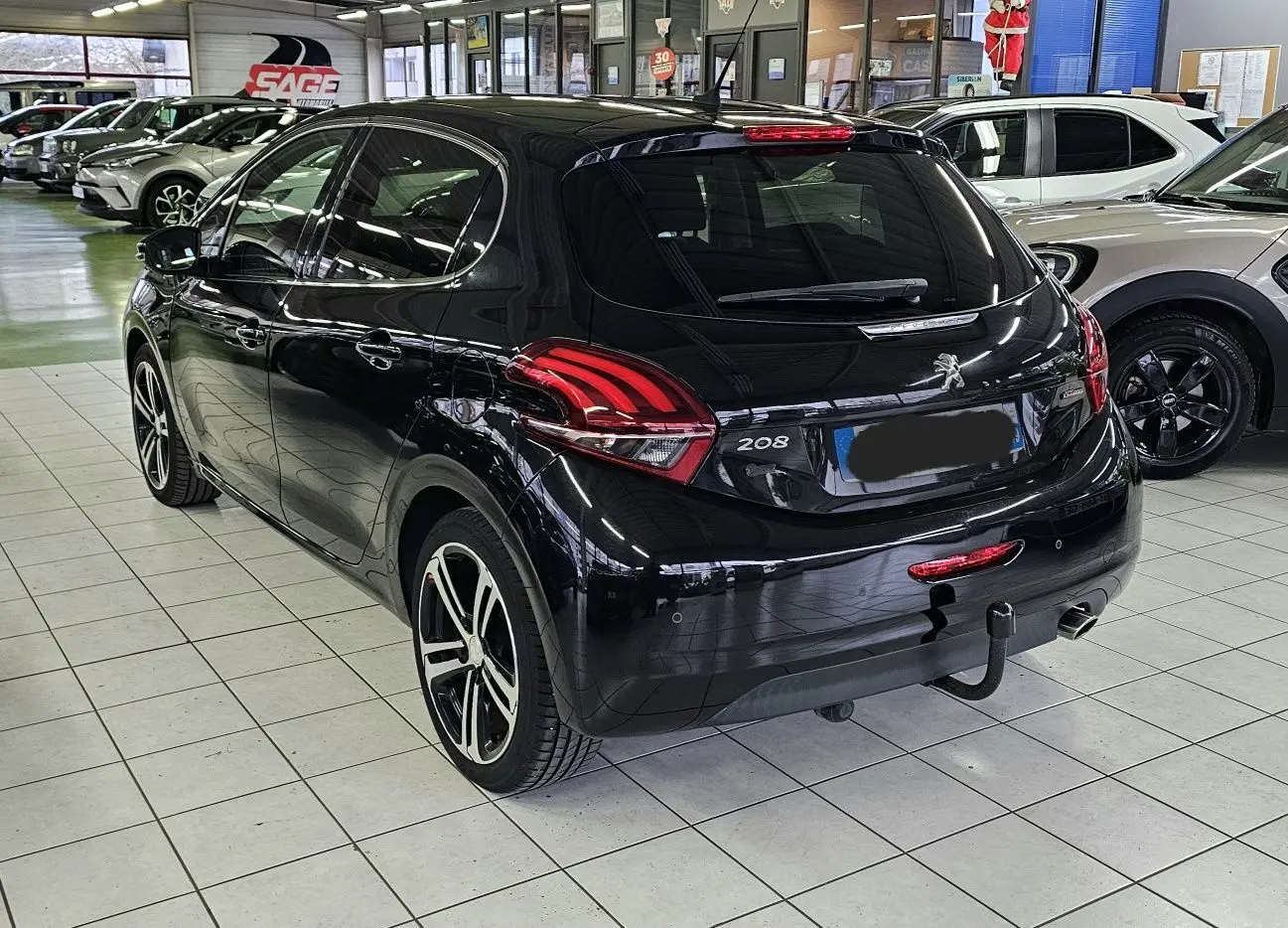 Vue 3/4 arrière droite d’une Peugeot 208 GT-LINE noire avec jantes alliage et attelage en concession.