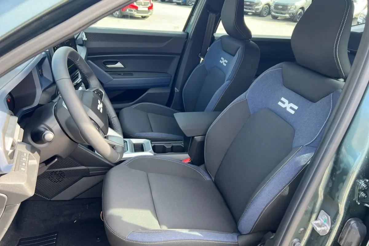 Intérieur avant du Dacia Bigster vert cèdre, sièges tissu noir et bleu avec logo DC, volant cuir visible côté gauche.