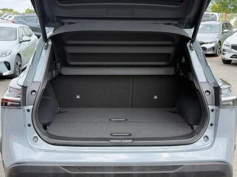 Coffre ouvert vu de l'arrière du Nissan Qashqai gris Argile 2025, montrant l'espace de chargement plat et les garnitures noires.