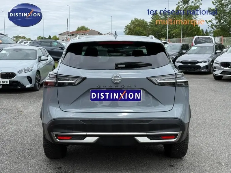 Vue arrière d'un Nissan Qashqai 2025 gris Argile avec feux arrière LED et barres de toit visibles sur parking.