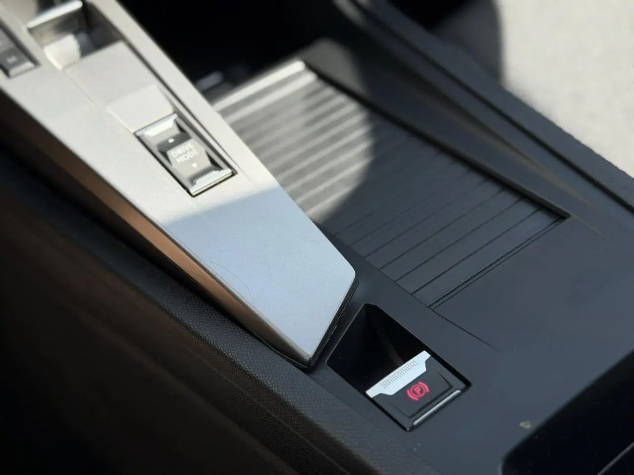Gros plan sur la console centrale noire avec bouton frein de parking électrique et commande Drive Mode dans une Peugeot 308 gris Artense.